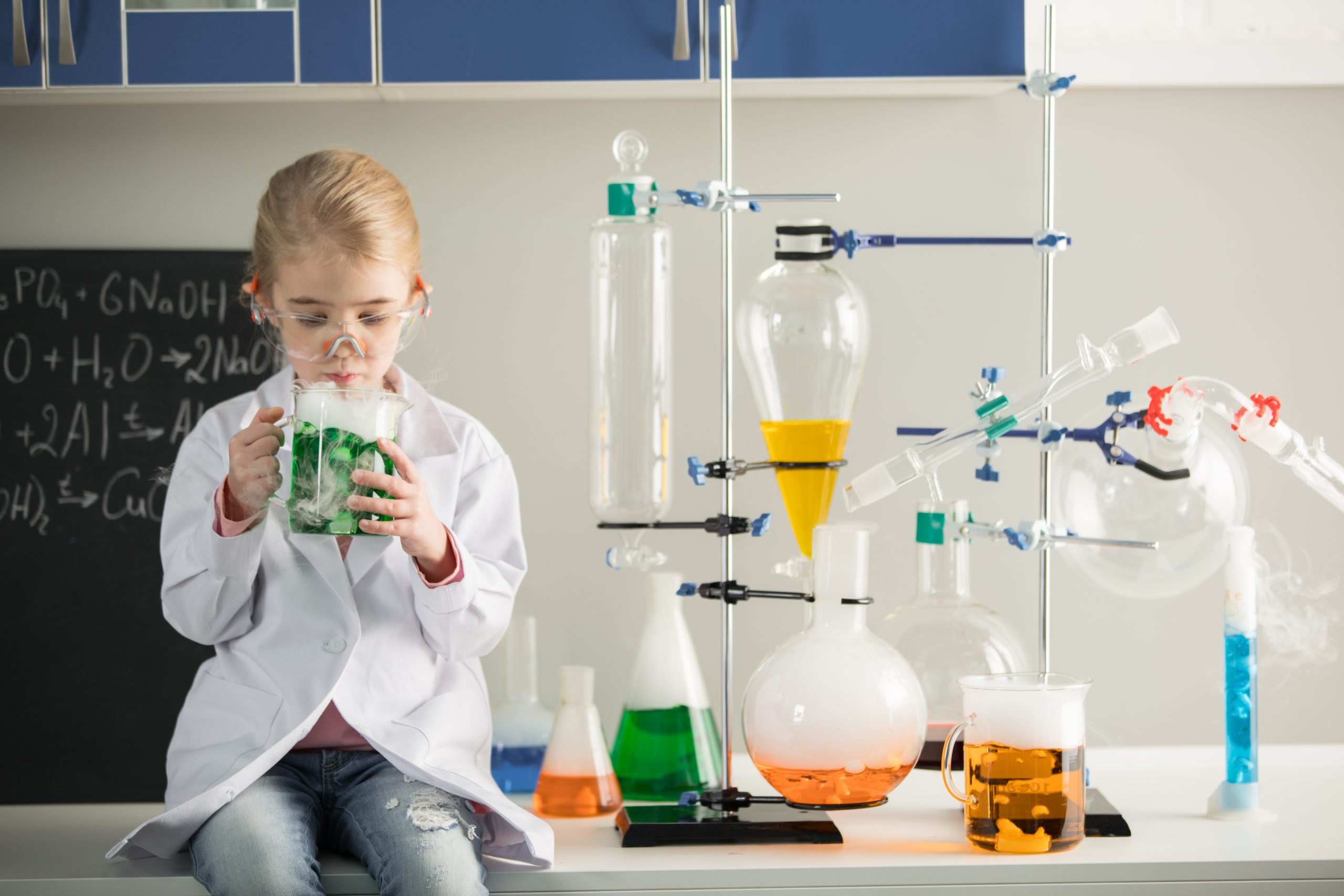 Schoolgirl holding flask with chemical sample while sitting in lab