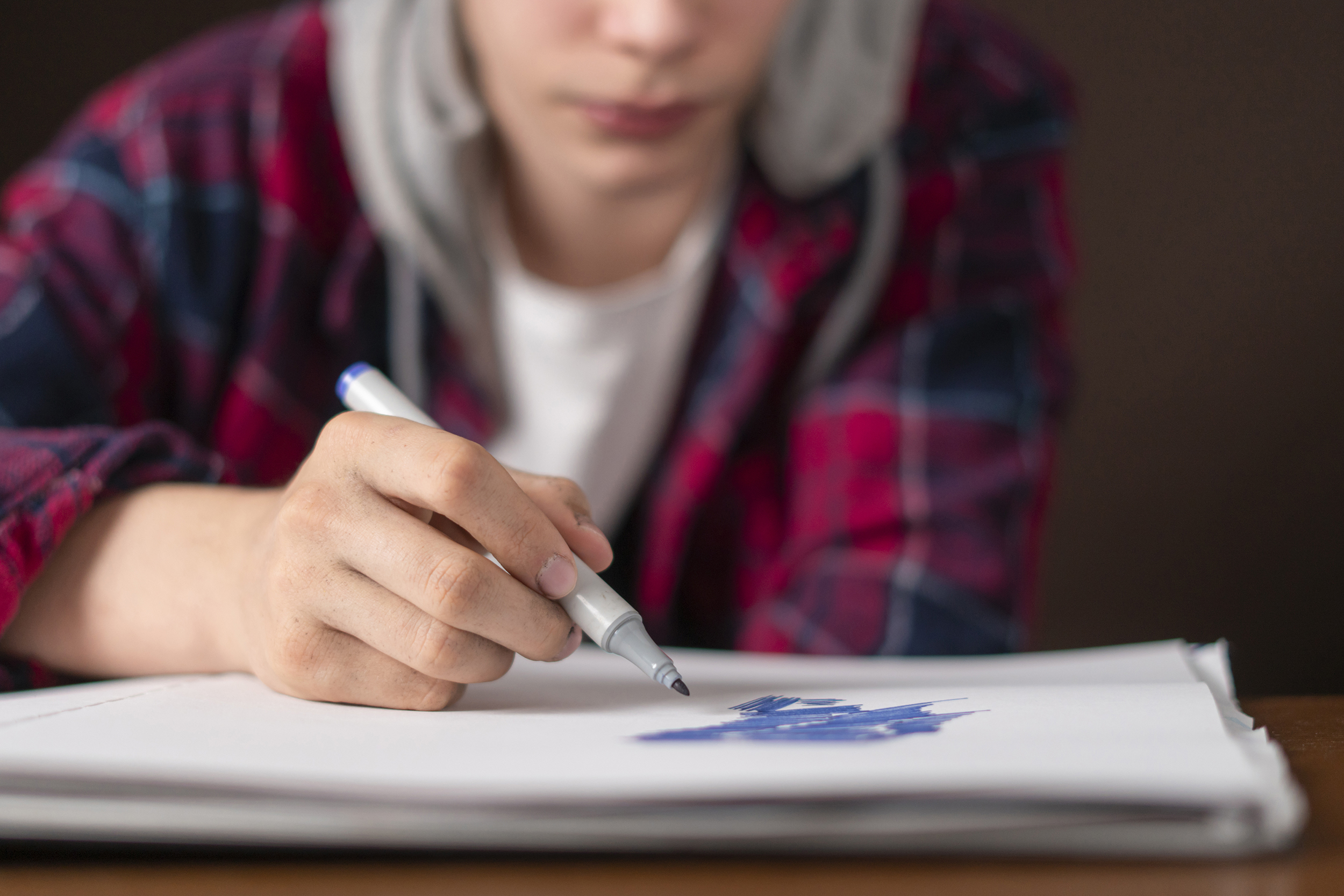 young male sitting at the table and drawing pictures in his notebook with marker b